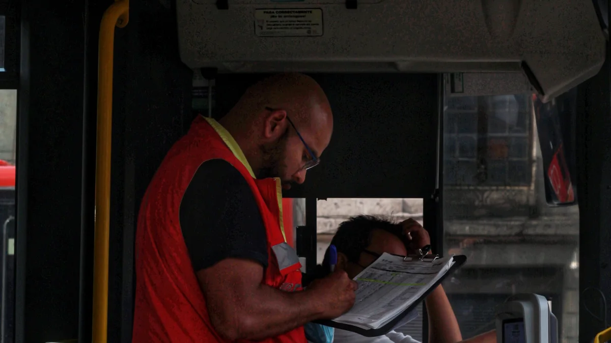Trabalhador de transporte confere uma prancheta na entrada de um ônibus